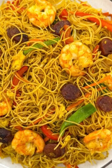 Singapore-style rice vermicelli stir-fried with shrimp, sliced sausage, egg, and peppers on a white plate.